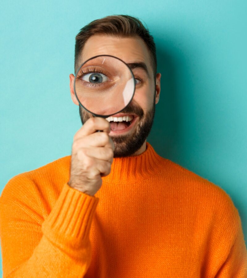 Smiling youth holding magnifying glass against turquoise background, symbolizing focus, curiosity, and self-driven career preparation through Identity Career kits.