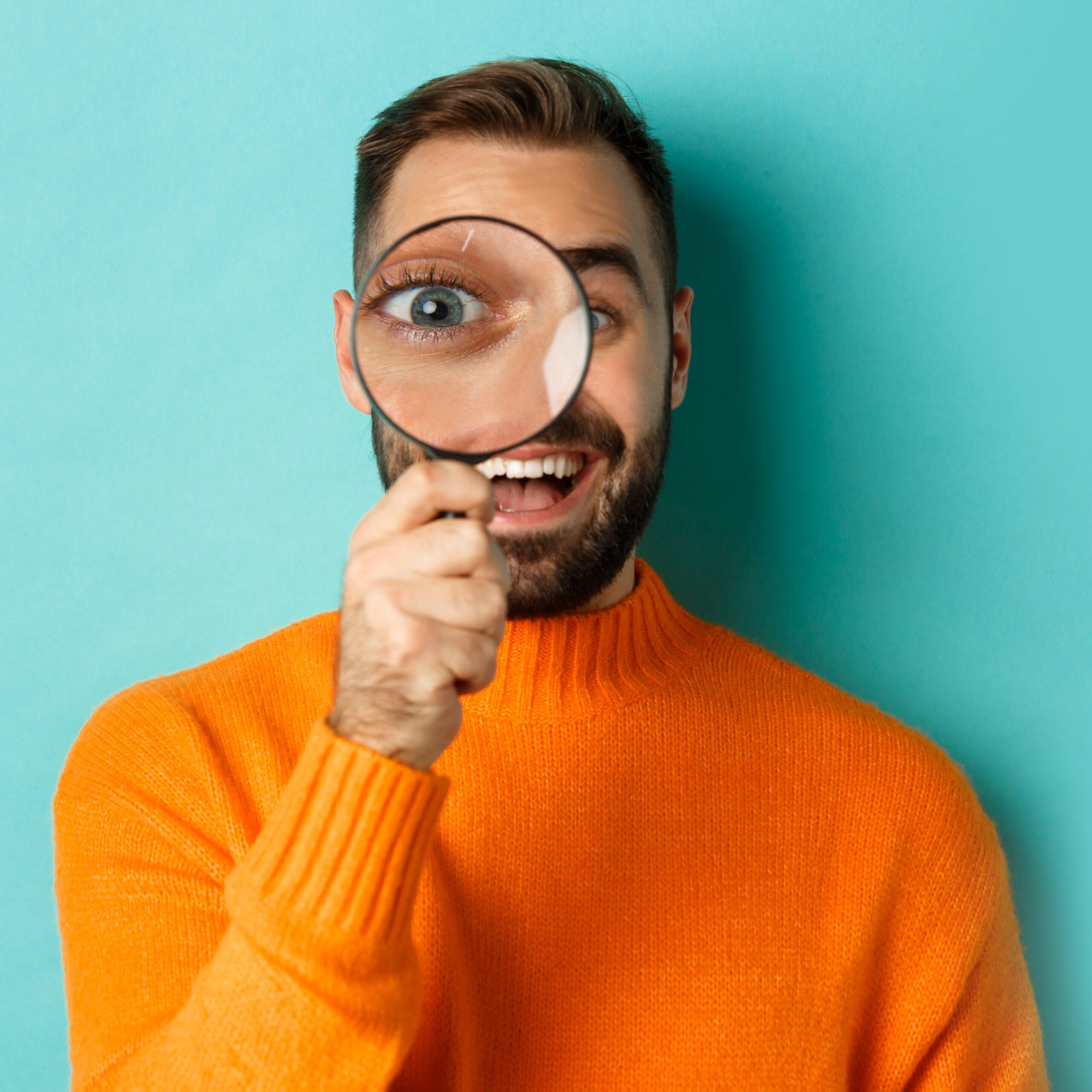 Smiling youth holding magnifying glass against turquoise background, symbolizing focus, curiosity, and self-driven career preparation through Identity Career kits.
