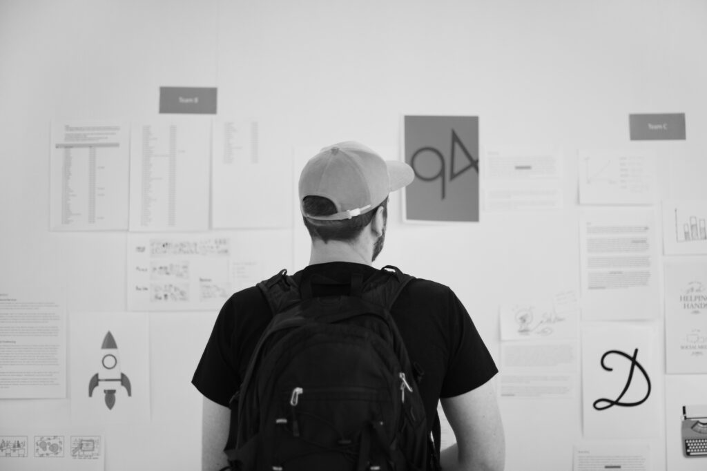 A young person stands in front of a wall covered with papers, diagrams, and symbols—absorbing ideas, searching for meaning, and exploring possibilities. The scene evokes the emotional tension of identity exploration and the pressure of early career decisions.