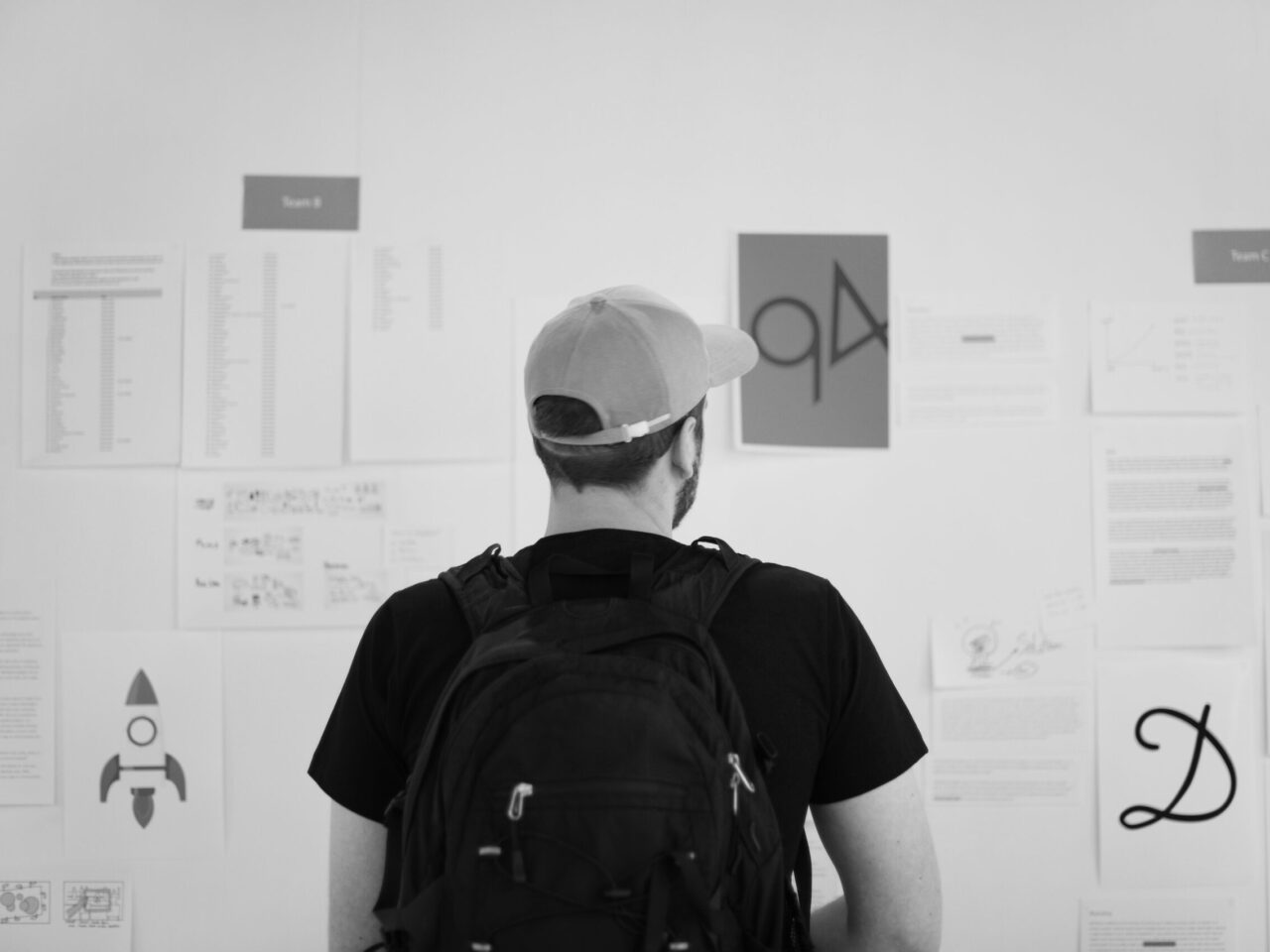 A young person stands in front of a wall covered with papers, diagrams, and symbols—absorbing ideas, searching for meaning, and exploring possibilities. The scene evokes the emotional tension of identity exploration and the pressure of early career decisions.
