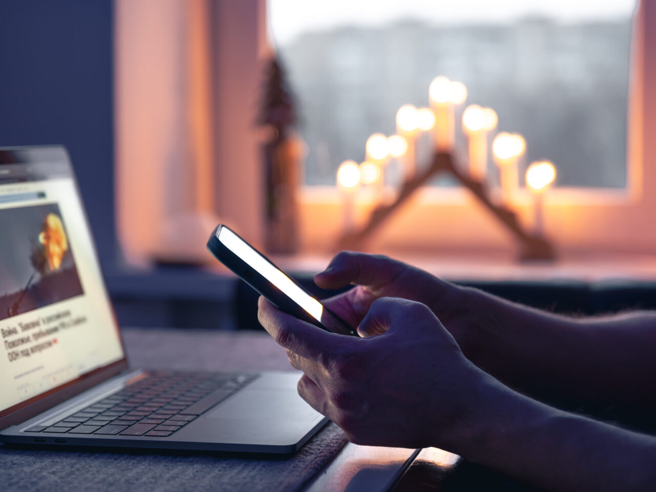 A professional using a smartphone and laptop at night, representing online presence and digital identity.