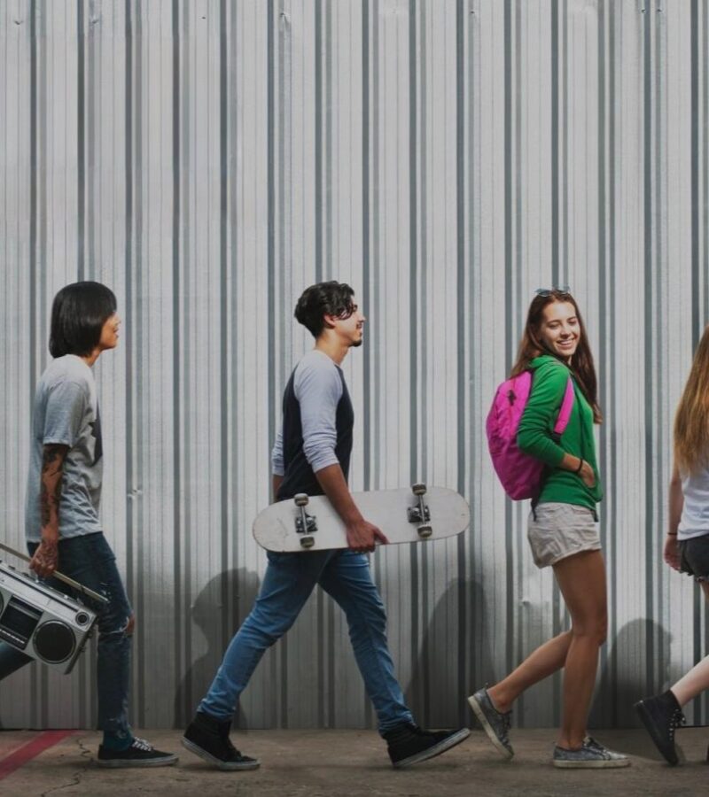 Five diverse youth walking confidently in front of a metal wall, symbolizing individuality, movement, and personal growth through Identity Career trainings and review services.